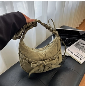 Detail of olive green nylon bag featuring a large bow and pleated scrunchie shoulder strap