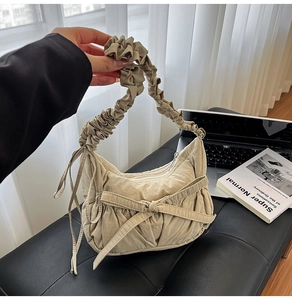 Detail of beige nylon pleated handbag featuring a large decorative bow and zip closure