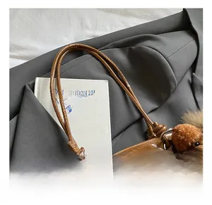 Détail d'un cabas marron brillant avec doubles anses et pendentif en peluche ours