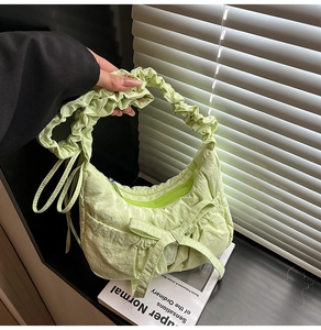 Detail of light green nylon shoulder bag featuring decorative bow and pleated cloud strap