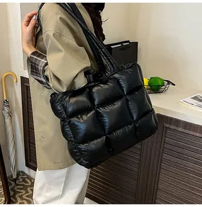 Detail of a large black quilted puffer tote bag shown on a shoulder in a lifestyle setting