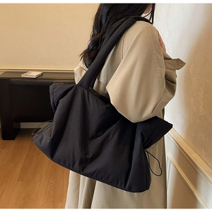 Détail d'un sac cabas noir matelassé avec cordons latéraux porté à l'épaule par un mannequin