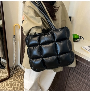 Detail of black quilted tote bag with glossy finish and square padded texture in use