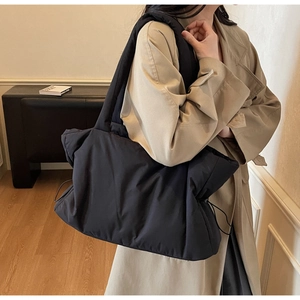 Detail of a black quilted nylon tote bag with drawstring features and wide shoulder strap