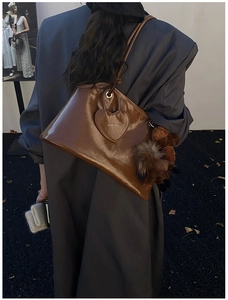 Détail d'un sac cabas marron avec patch cœur et breloque peluche dans un cadre mode