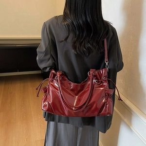 Minimalist deep red patent leather tote bag with drawstring detail shown on a model