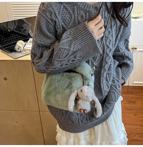 Détail d'un sac bandoulière en peluche verte avec chaîne et breloque lapin sur un bureau