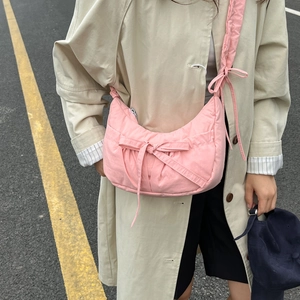 Pink crescent nylon crossbody bag with bow details worn by a model on a street background