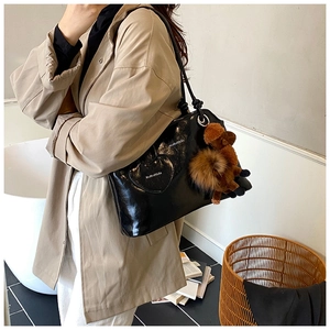 Dettaglio borsa tote in pelle cerata nera con ciondolo a cuore e peluche marrone