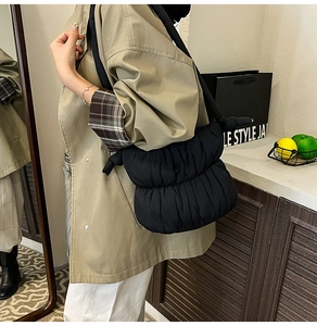 Detail of black quilted puffer bag in shiny nylon worn with a khaki trench coat