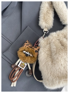 Detail of plush beige faux fur crossbody bag featuring a cute doll charm on a grey suit