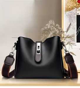 Gros plan du sac seau en cuir noir avec fermoir rotatif argenté et bandoulière marron