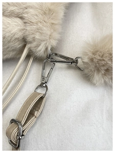 Detail of beige plush faux fur bucket bag with silver metal hooks and adjustable strap