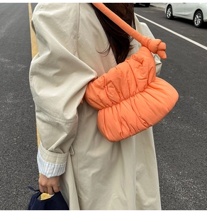 Outdoor street shot of an orange quilted puffy cloud bag with knotted strap detail