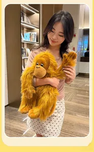 Close-up of a large golden long-haired orangutan plush toy held by a woman in a room