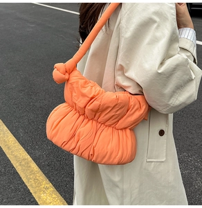 Detail of bright orange quilted puffer bag featuring a unique knotted shoulder strap