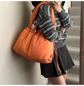 Detail of quilted orange puffer tote bag with knotted strap shown on person