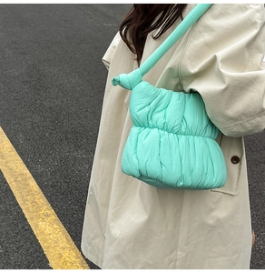 Detail of mint green quilted cloud bag with knot shoulder strap worn over a beige trench coat