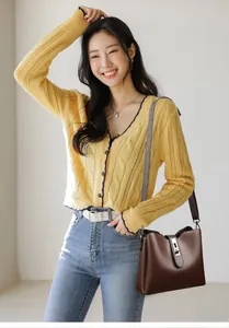 Détail du sac seau en cuir marron foncé avec boucle argentée sur cardigan jaune