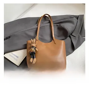 Detail of a brown leather tote bag with a knit rabbit charm on a stylish blazer