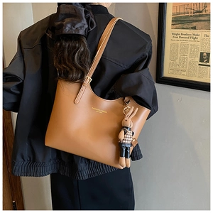 Brown leather tote bag with rabbit charm shown on model in urban casual setting