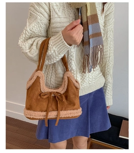 Detail of suede bucket bag featuring beige faux shearling trim and decorative bow knot