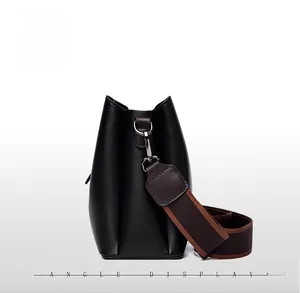 Vue latérale du sac seau en cuir noir avec large bandoulière en tissu rayé marron