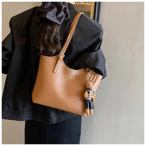 Detail view of brown leather tote bag with fashion text and cute rabbit pendant on strap