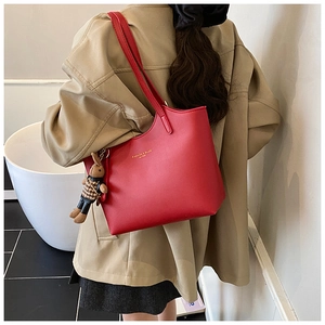 Detail of red leather tote bag with fashion logo and cute rabbit charm on shoulder
