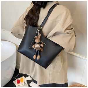 Detail of a black leather tote bag featuring a cute plush bunny charm and golden logo