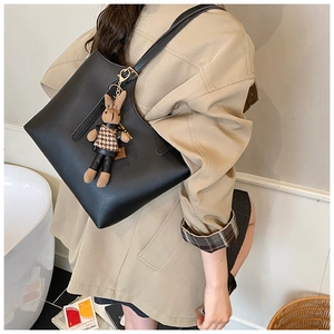 Close-up of a black leather tote bag featuring a cute brown rabbit plush charm detail