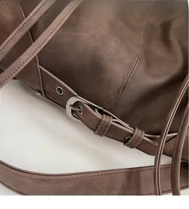Detail of a brown leather shoulder bag featuring silver buckle and adjustable strap