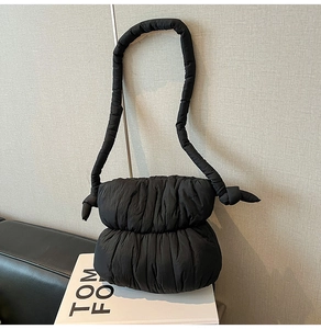Detail of black quilted puffer shoulder bag with stylish knot strap and soft puffy texture
