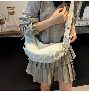 Close-up of minimalist off-white dumpling bag with textured nylon and wide strap