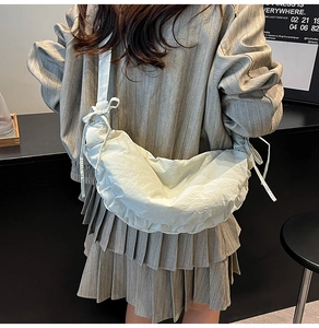Close-up of beige crescent dumpling bag with pleated texture and bow drawstring detail