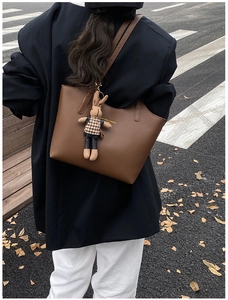 Detailed view of deep brown tote bag with cute plush rabbit charm on a houndstooth top