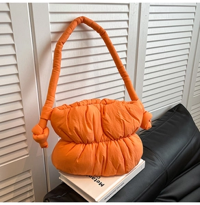 Detailed view of quilted orange puffer cloud bag with knot details on white books