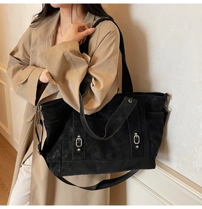 Detail of black large capacity tote bag with adjustable silver buckles on a trench coat