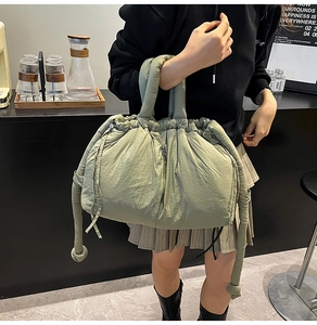 Detail of sage green puffer tote bag featuring drawstring closure and side zipper pocket