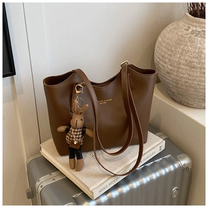 Detailed view of a brown leather tote bag with a golden logo and a cute bunny charm