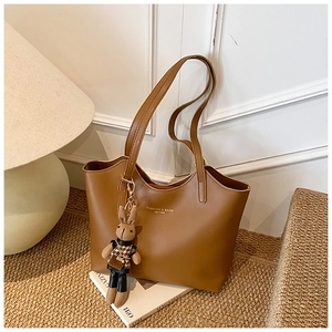 Detailed side view of a brown tote bag with a plush rabbit charm on a woven rug