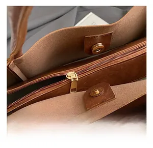 Detail of a brown leather tote bag showing gold zipper pocket and magnetic snap closure