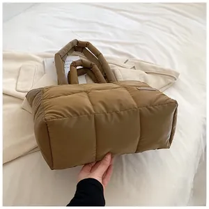 Detail of coffee brown quilted down tote bag with wide padded straps on white linen