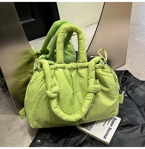 Macro view of bright green quilted nylon tote with knotted handle on a black leather background