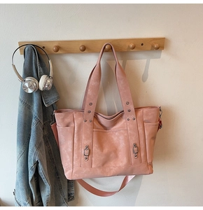 Pink vintage canvas tote bag with metal rivets and side pockets hanging on a hook