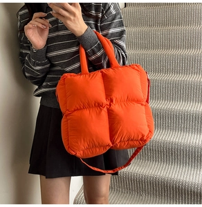 Detail view of a bright orange quilted puffer handbag with padded handles and strap