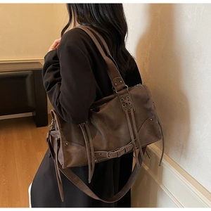 Detail of dark brown tote bag featuring matte texture, metal rivets, and moto style buckles