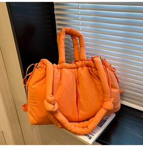Detail of bright orange quilted puffer bucket bag with drawstring and padded handle
