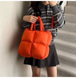 Detail of a large orange quilted puffer bag with thick handle and stylish padded texture