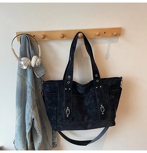 Detail of vintage black canvas tote bag showing washed texture and metal rivets on a rack